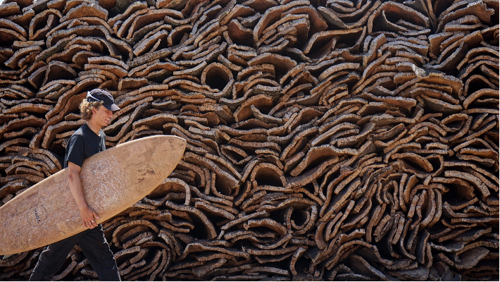 Shaper with a Hara cork surfboard in front of stacked cork bark